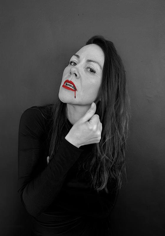 Black and white headshot of a woman with bright red lipstick with a blood stain dripping down her chin.