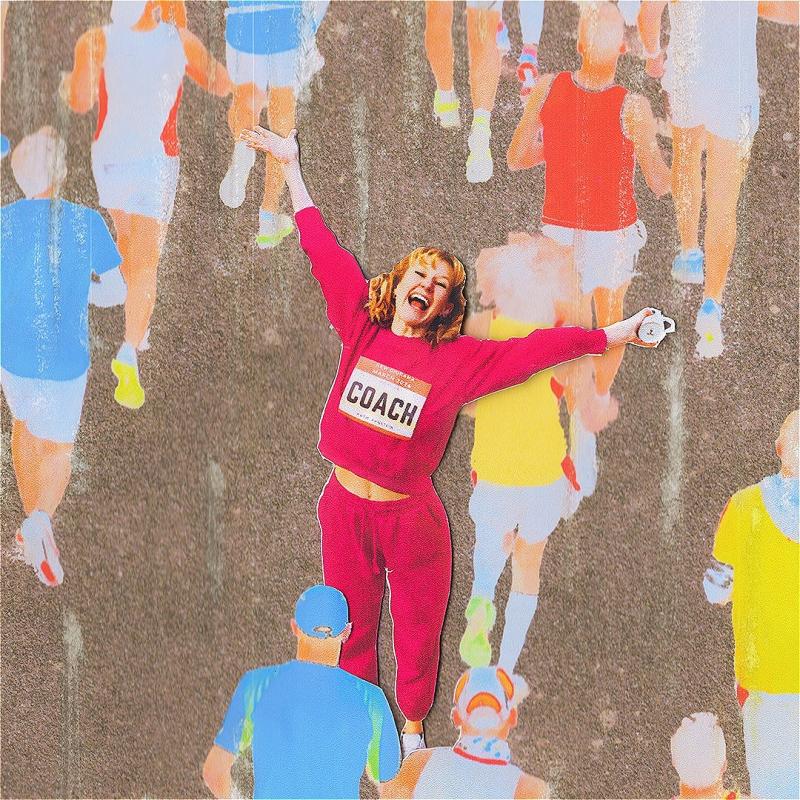 A woman wearing a pink tracksuit celebrates as people run past her.