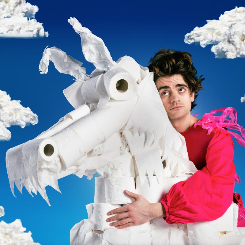 Luke cradles a unicorn made out of toilet paper with blue skies in the background.