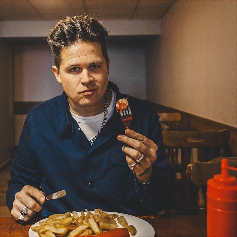 A man eating sausage and chips, wearing a blue shirt.