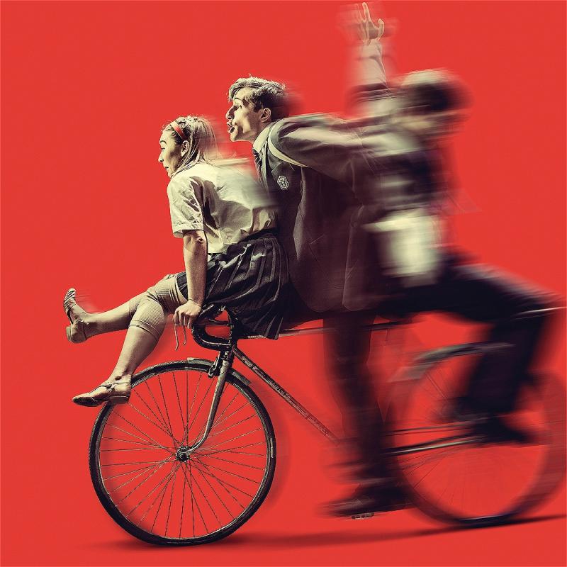 A blurred image depicting a bicycle and three figures in front of a red background.