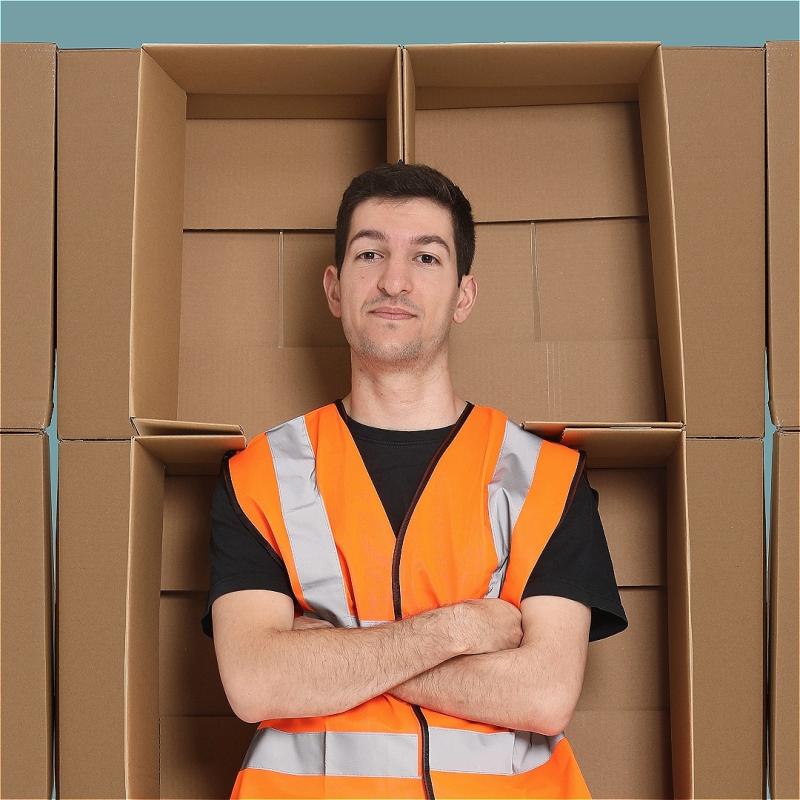 A man standing in front of cardboard boxes, wearing a high-vis jacket with his arms folded.