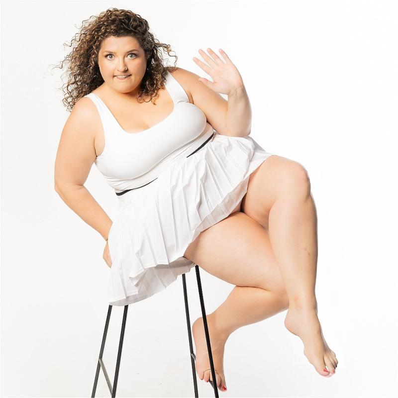 Woman sitting on a stool in a white dress, holding her hand up.