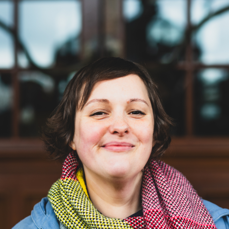 Josie Long looking straight at the camera in front of reflective door window and smiling