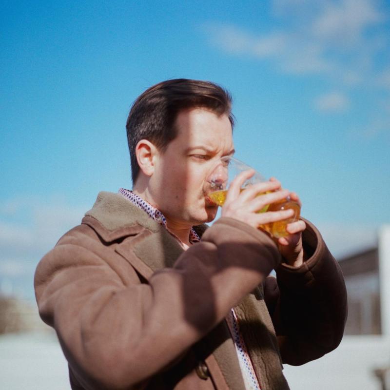 Andy drinking a pint intently outside against a blue sky.