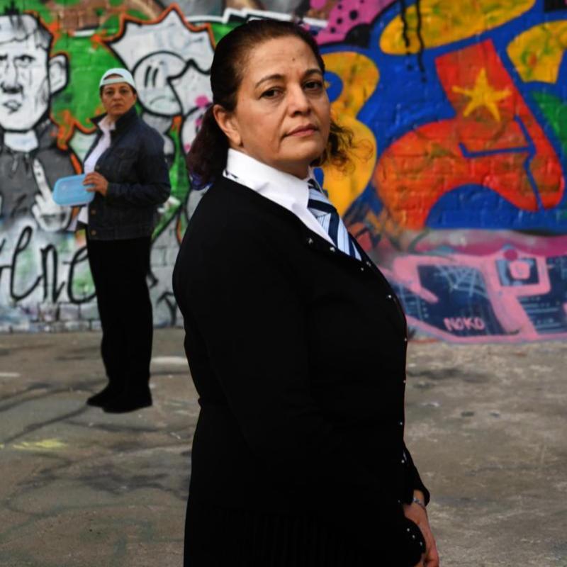 The actor standing in front of a graffiti wall in school uniform. The other character stands apart in the back.