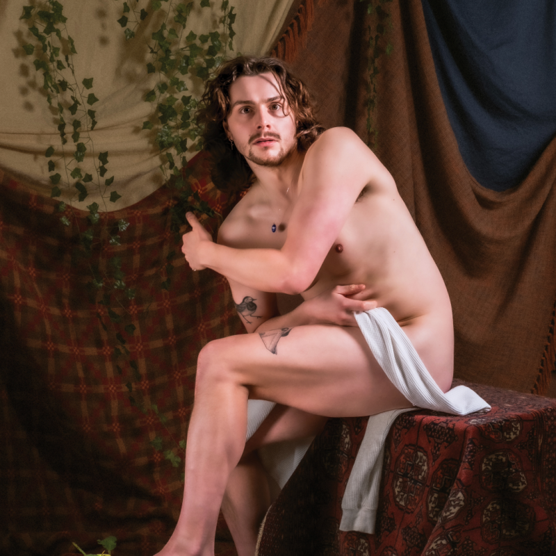 Sam looking startled whilst naked with a white shawl covering their modesty.