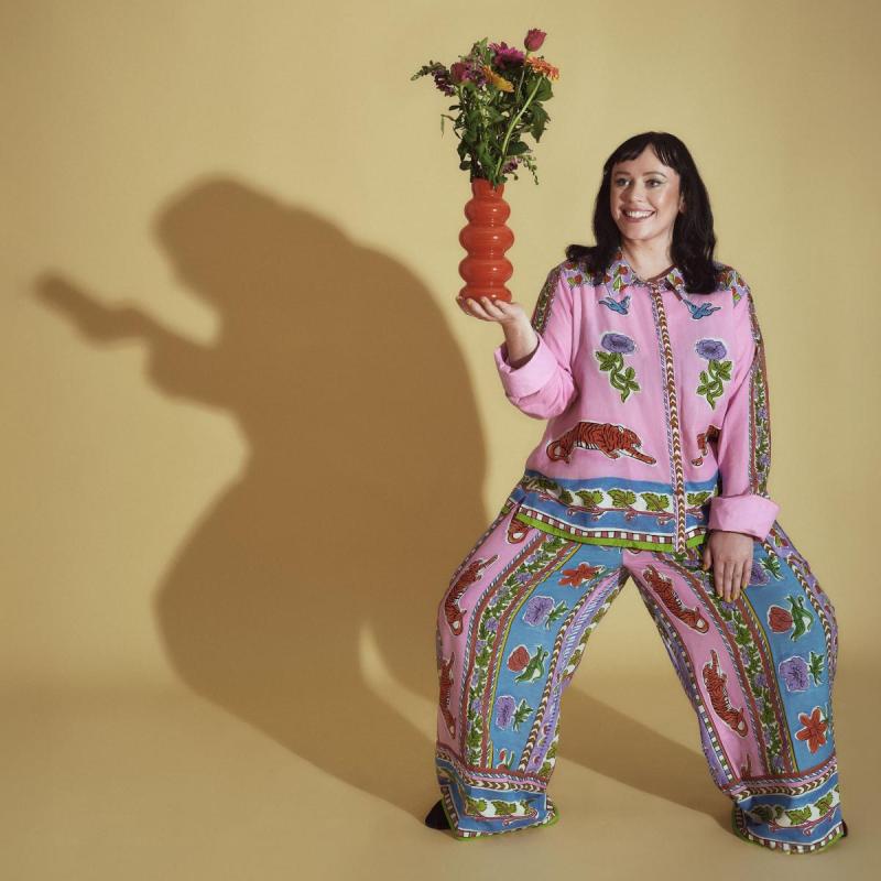 Amy Annette holding a vase with flowers in a printed outfit with her legs apart
