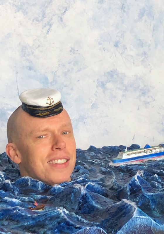 A man's head floating in a body of water with a ship in the background