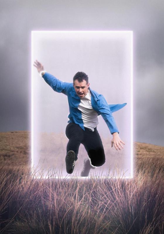 Man in blue shirt leaping through a neon box on a hillside