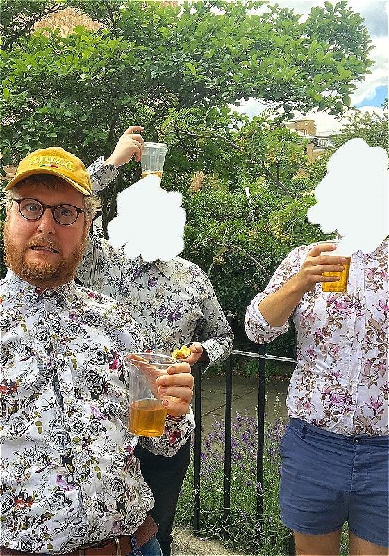 Tim Key in a printed paisley shirt holding a pint glass in a garden. Two friends behind him, with their faces blurred out.