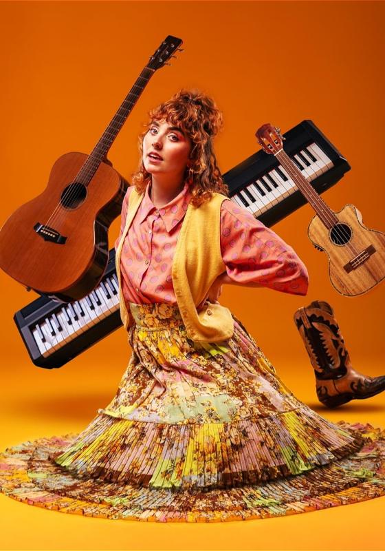 Annabel wears different tones of orange and knees on the orange floor, surrounded by instruments .