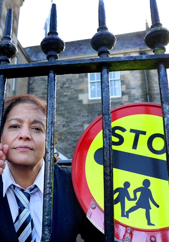 Person in a suit standing behind a gate with a 'STOP' children crossing sign.