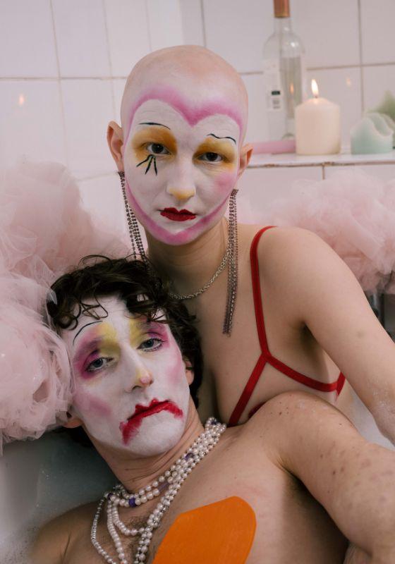 Two clowns in cabaret make-up sit in a bath tub.