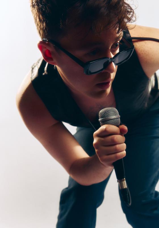 The performer in a waistcoat and trousers, holding a microphone and wearing sunglasses.