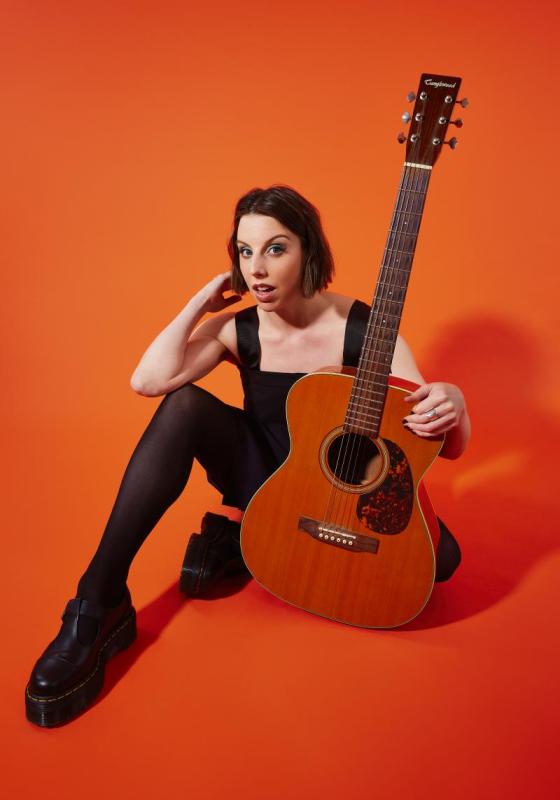 A person sat holding a guitar against an orange background.