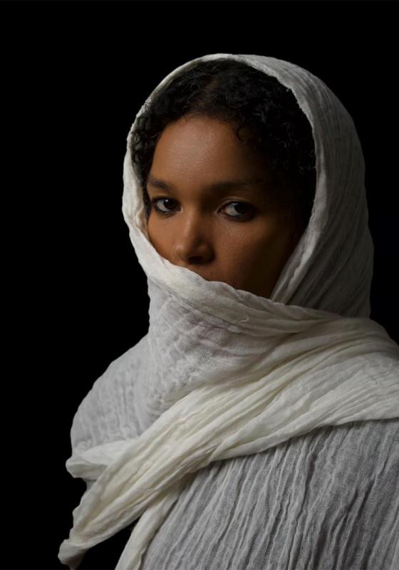 Person in white headscarf against a black background.