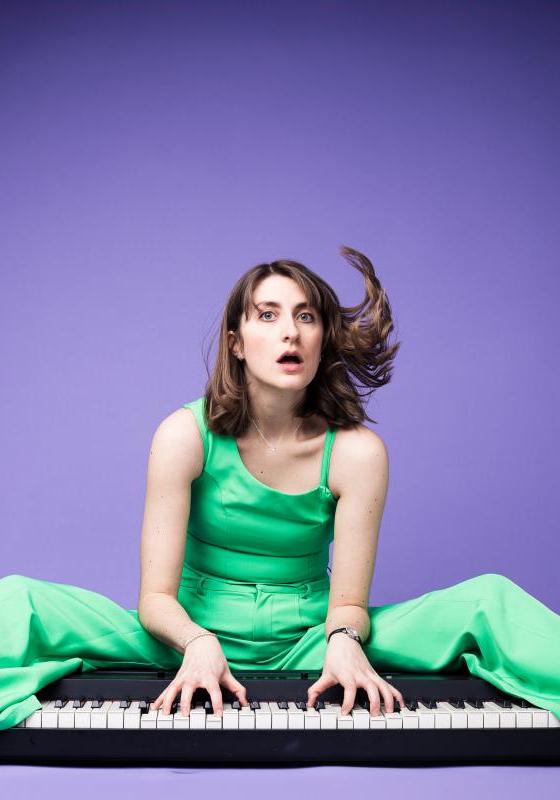 Image of Anna Hale, performer, playing a keyboard in front of a purple background