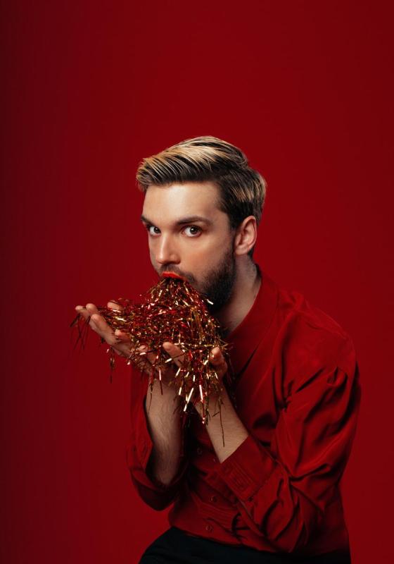 Image of Will Owen, performer, eating confetti in front of a red background