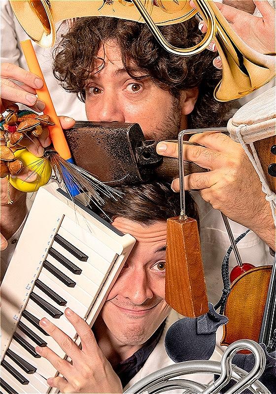 Two men wearing white lab coats, pulling happy, funny faces and carrying an array of instruments on a pink background