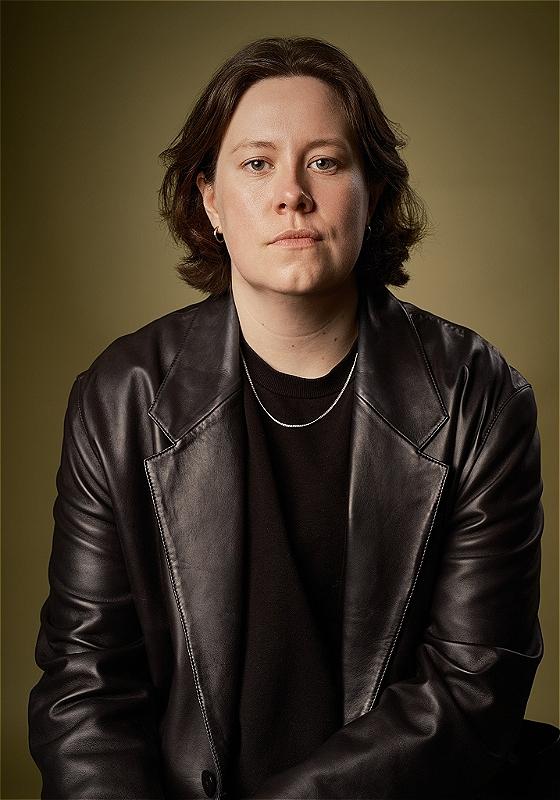 Chloe Petts stares at the camera in a black leather jacket, black t-shirt and silver chain.