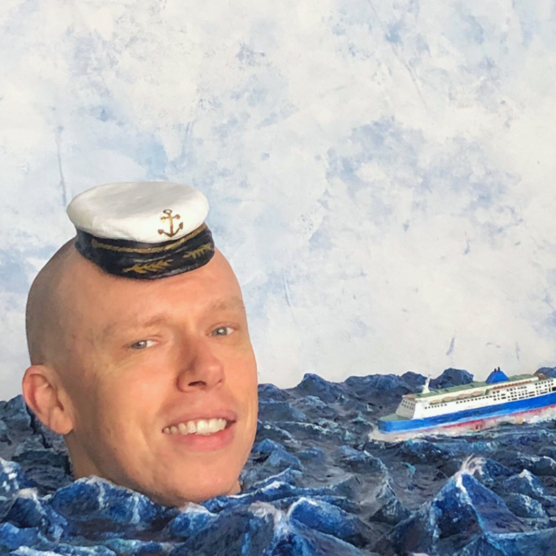 A man's head floating in a body of water with a ship in the background