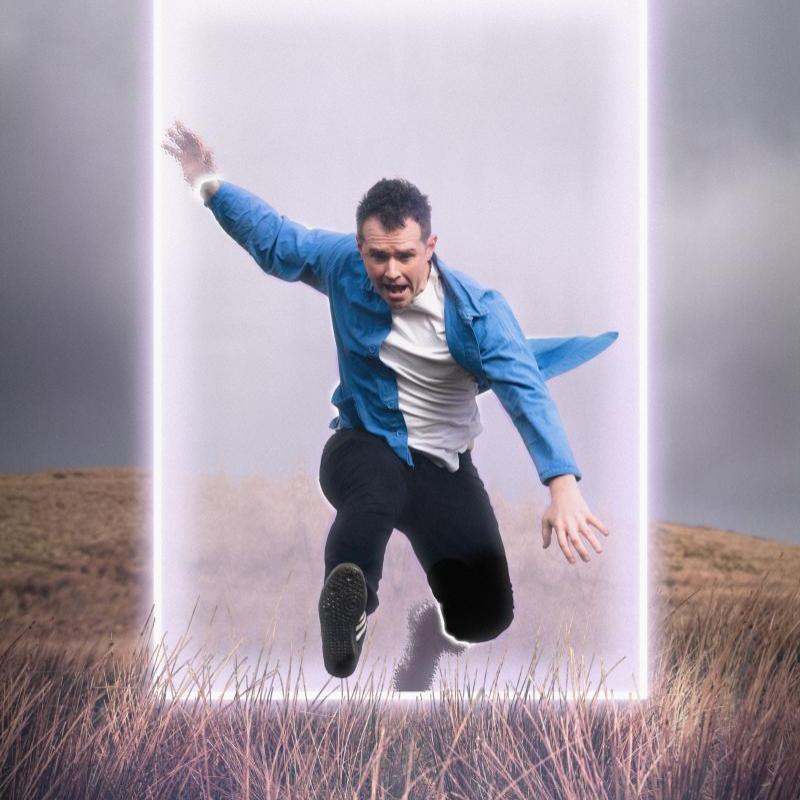 Man in blue shirt leaping through a neon box on a hillside