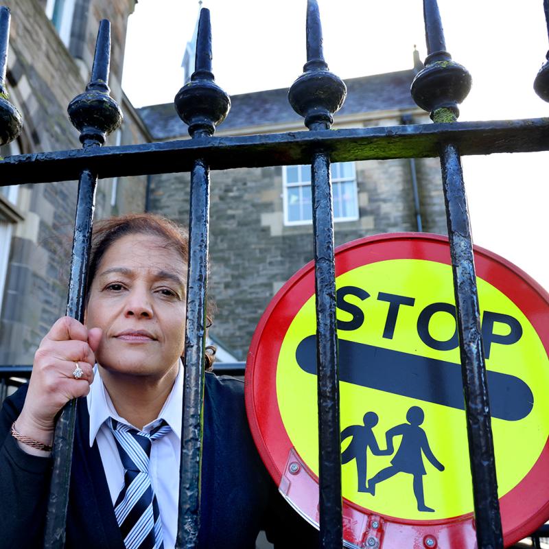 Person in a suit standing behind a gate with a 'STOP' children crossing sign.