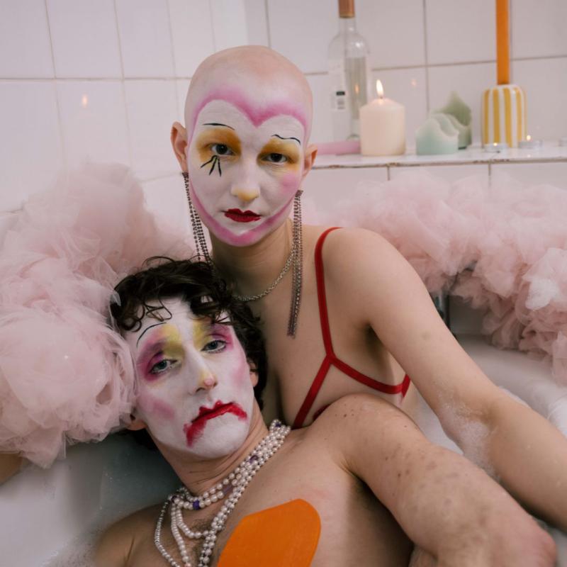 Two clowns in cabaret make-up sit in a bath tub.