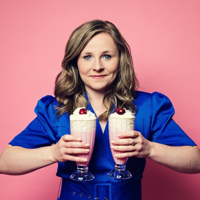 A person in a blue dress holding 2 glasses of milkshake