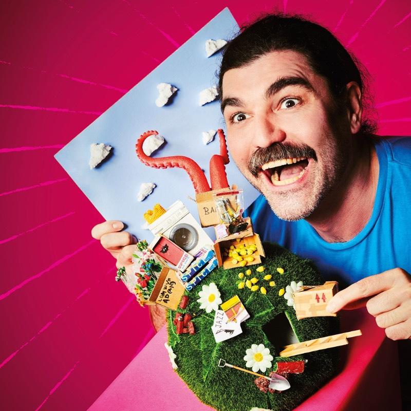 John Luke Roberts holds up a grass covered globe and points to miniatures of his show.