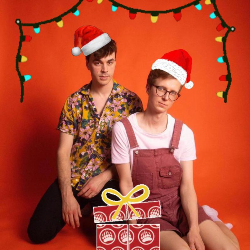 Two people wearing santa hats and sitting on a red background