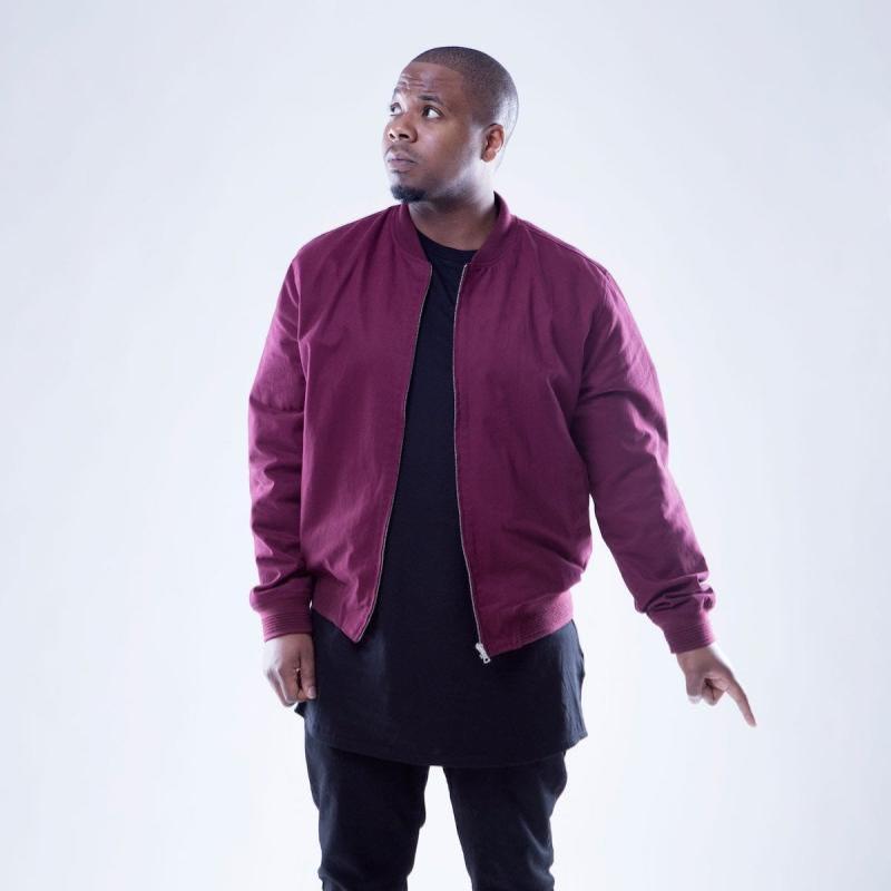 Full length photo of Marlon wearing black trousers, a black t-shirt, maroon trainers and a matching jacket.