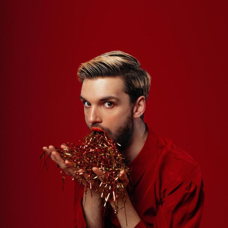 Image of Will Owen, performer, eating confetti in front of a red background