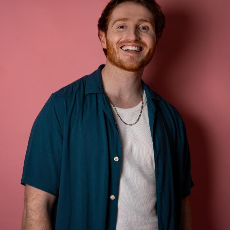 Ali smiling at the camera against a pink backdrop