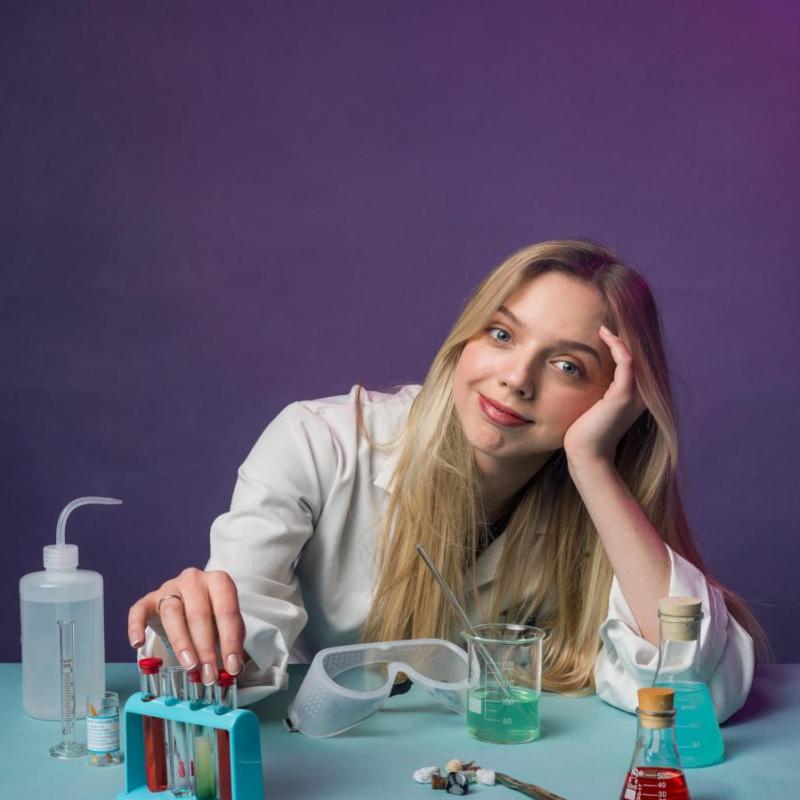 Freya smiles at the camera wearing a lab coat and surrounded by scientific apparatus