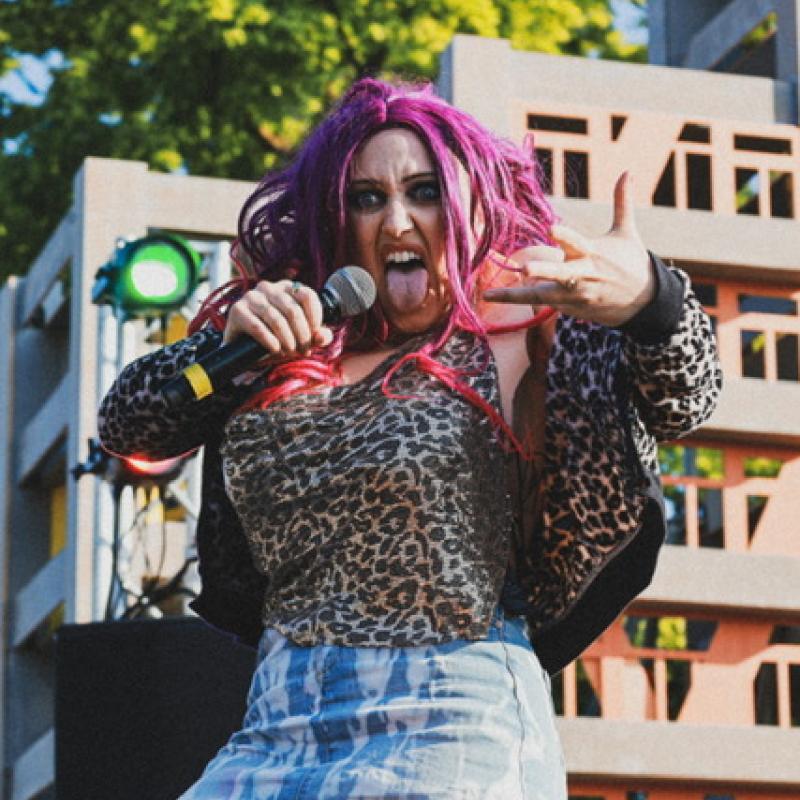 A person with purple hair and pink hair holding a microphone