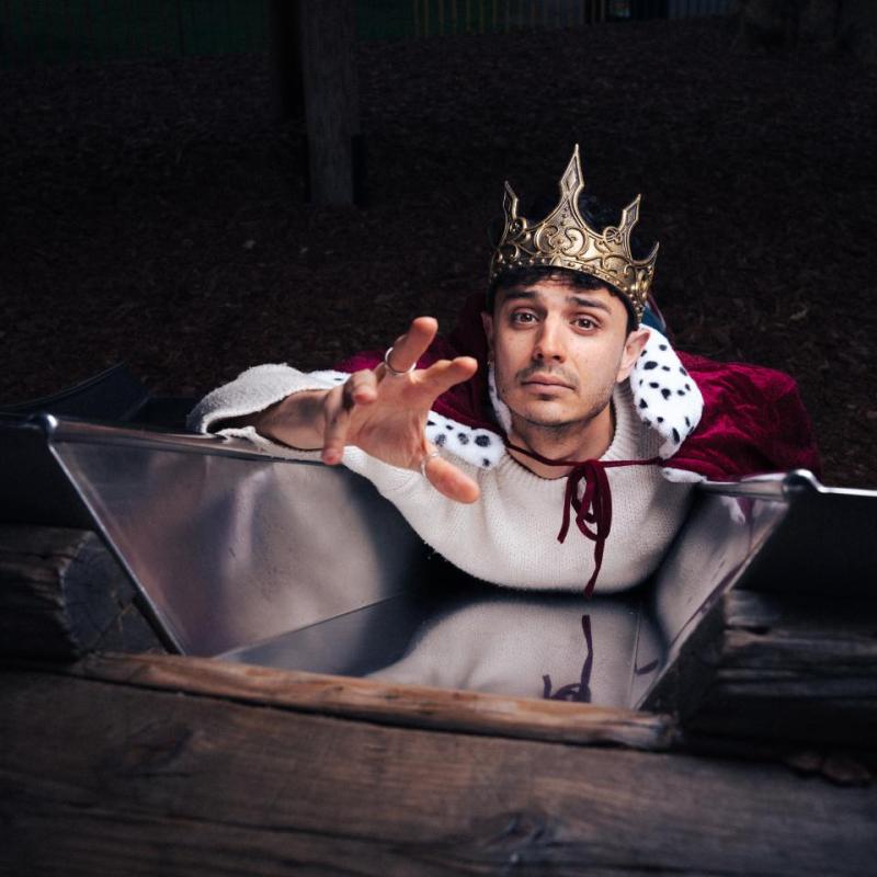 A person wearing a crown and lying in a metal tub