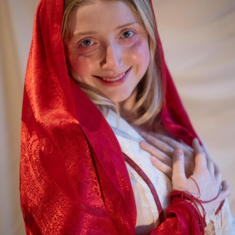 Bebe grinning at the camera wearing a long red cloak