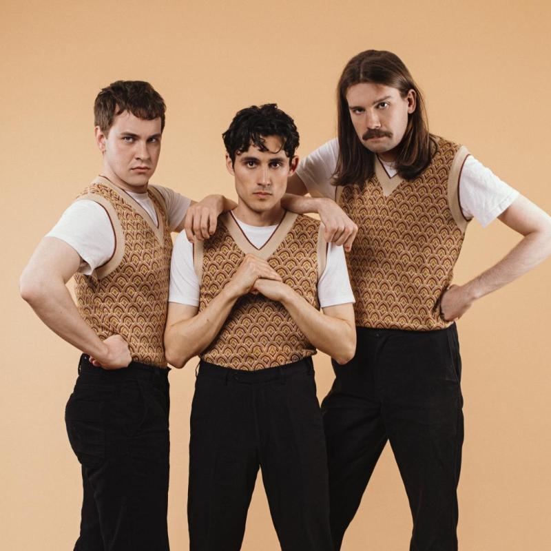 The cast of Crybabies wearing matching patterned sweater vests and black trousers looking menacingly at the camera.