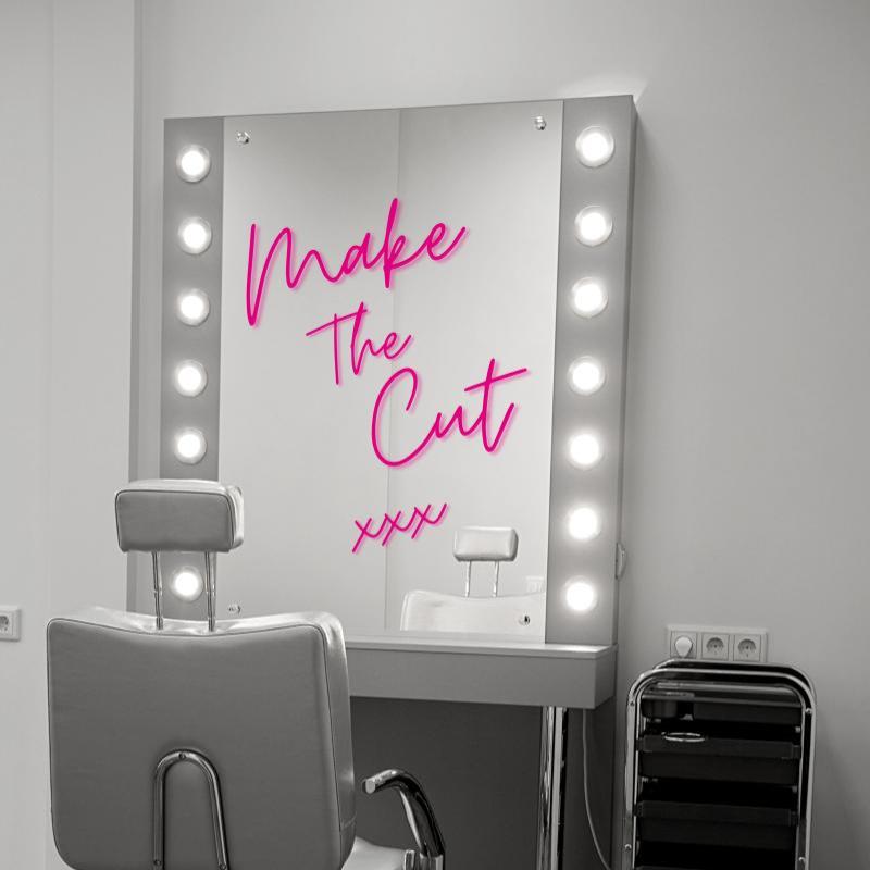 Black and white image of a makeup chair and makeup mirror with lights around it. The words 'Make The Cut xxx' are written in pink on the mirror/ 