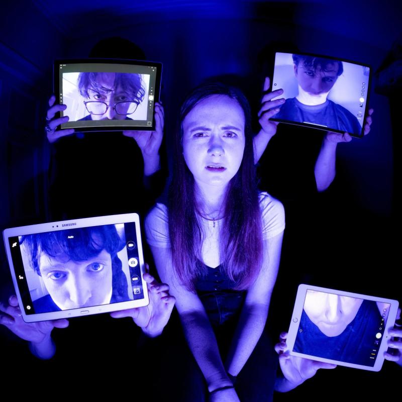 A girl with a bewildered expression surrounded by 4 screens with men's faces on under a backlight