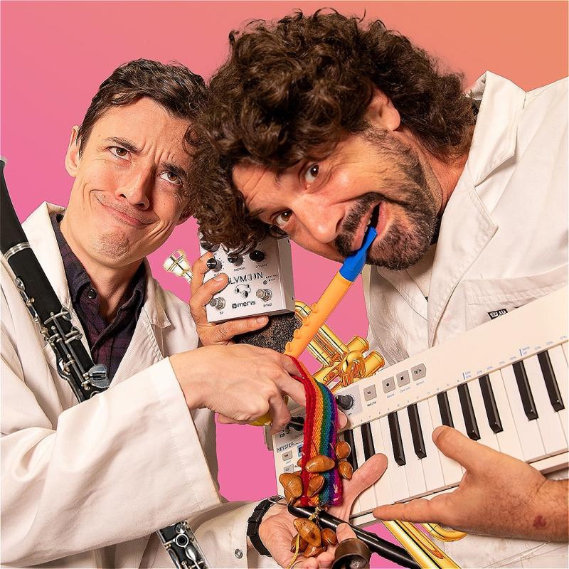 Two men wearing white lab coats, pulling happy, funny faces and carrying an array of instruments on a pink background