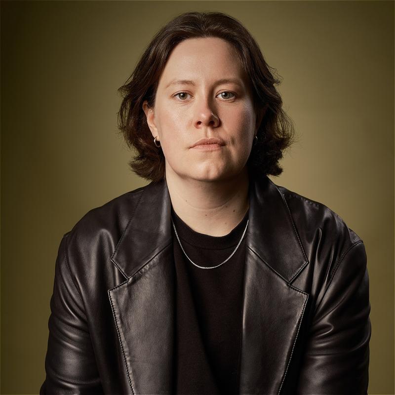 Chloe Petts stares at the camera in a black leather jacket, black t-shirt and silver chain.